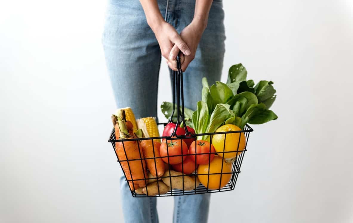 אישה מחזיקה סל קניות עם פירות וירקות