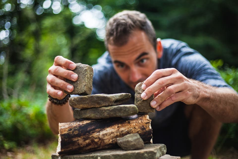 גבר צעיר בונה מבנה מאבנים ועצים ביער