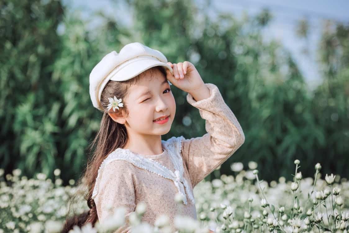 ילדה קטנה עם כובע בשדה של פרחים עושה קריצה עם העין