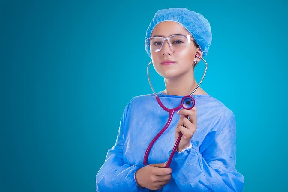 רופאה מרדימה בחלוק כחול ומשקפי מגן מחזיקה סטטוסקופ